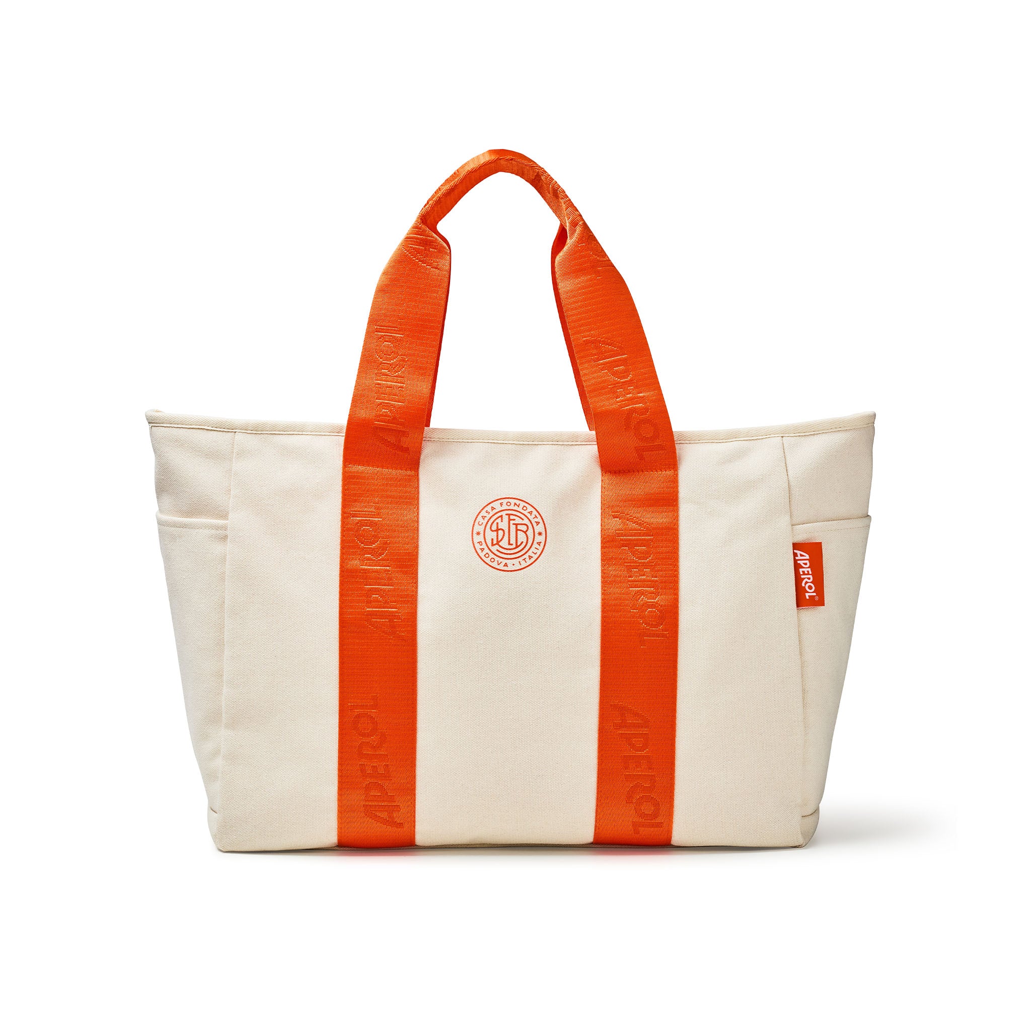 A cream canvas tote bag with bright orange webbed handles and vertical orange straps on the front, featuring a circular orange logo on the center and a small orange brand tag on the side, set against a plain white background.