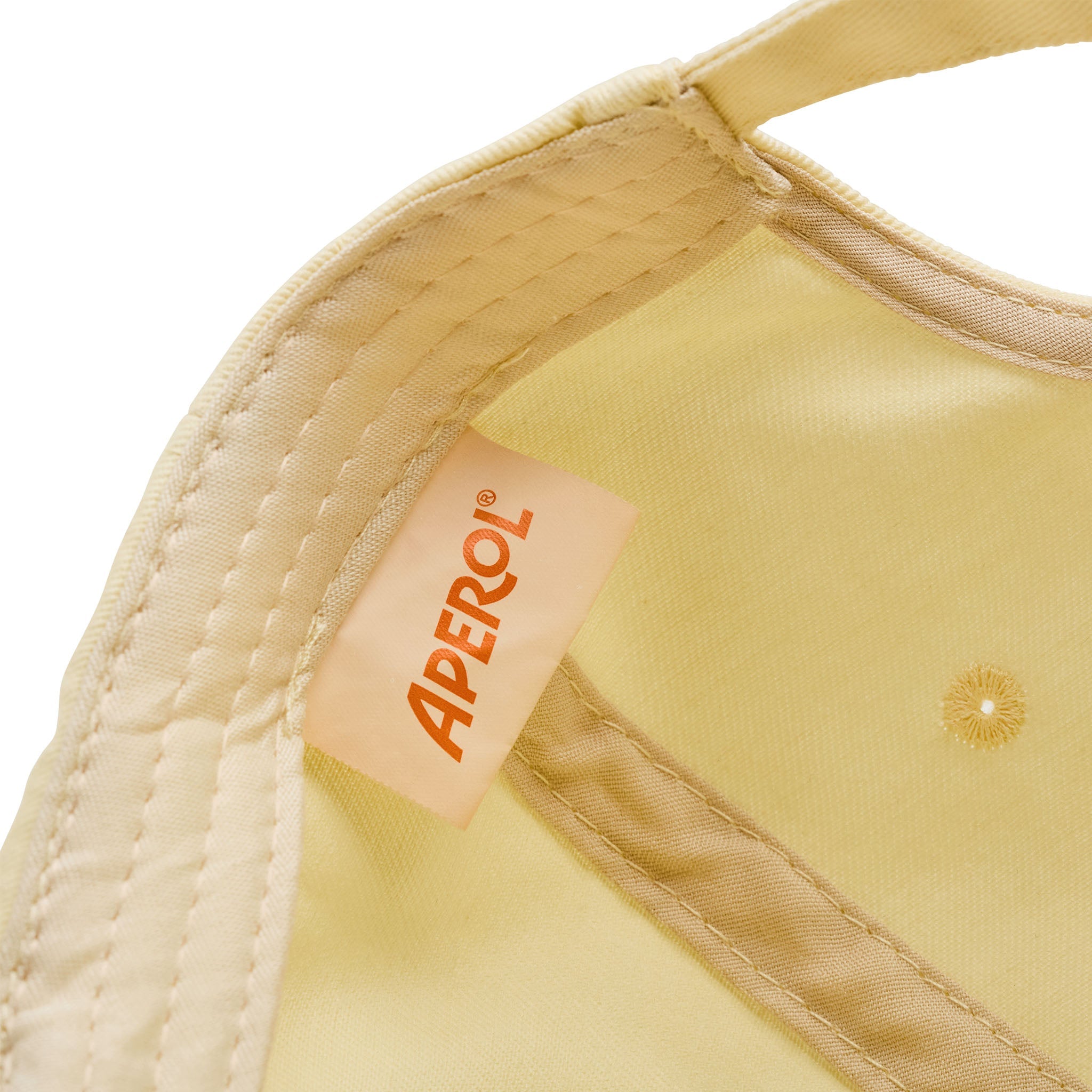 Close-up of a pale yellow fabric product with cream-colored stitching and a tan brand label reading APEROL.