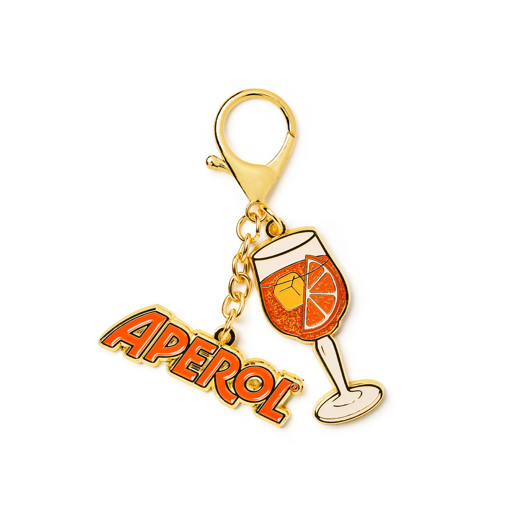 A gold-tone enamel keychain charm featuring the word 'APEROL' in orange and red gradient lettering, alongside an illustration of an aperol spritz cocktail glass with orange liquid and a slice of orange.