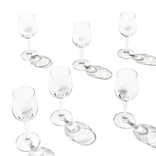 Six clear glasses with 'APEROL SPRITZ' branding, arranged on a white background with soft circular shadows.