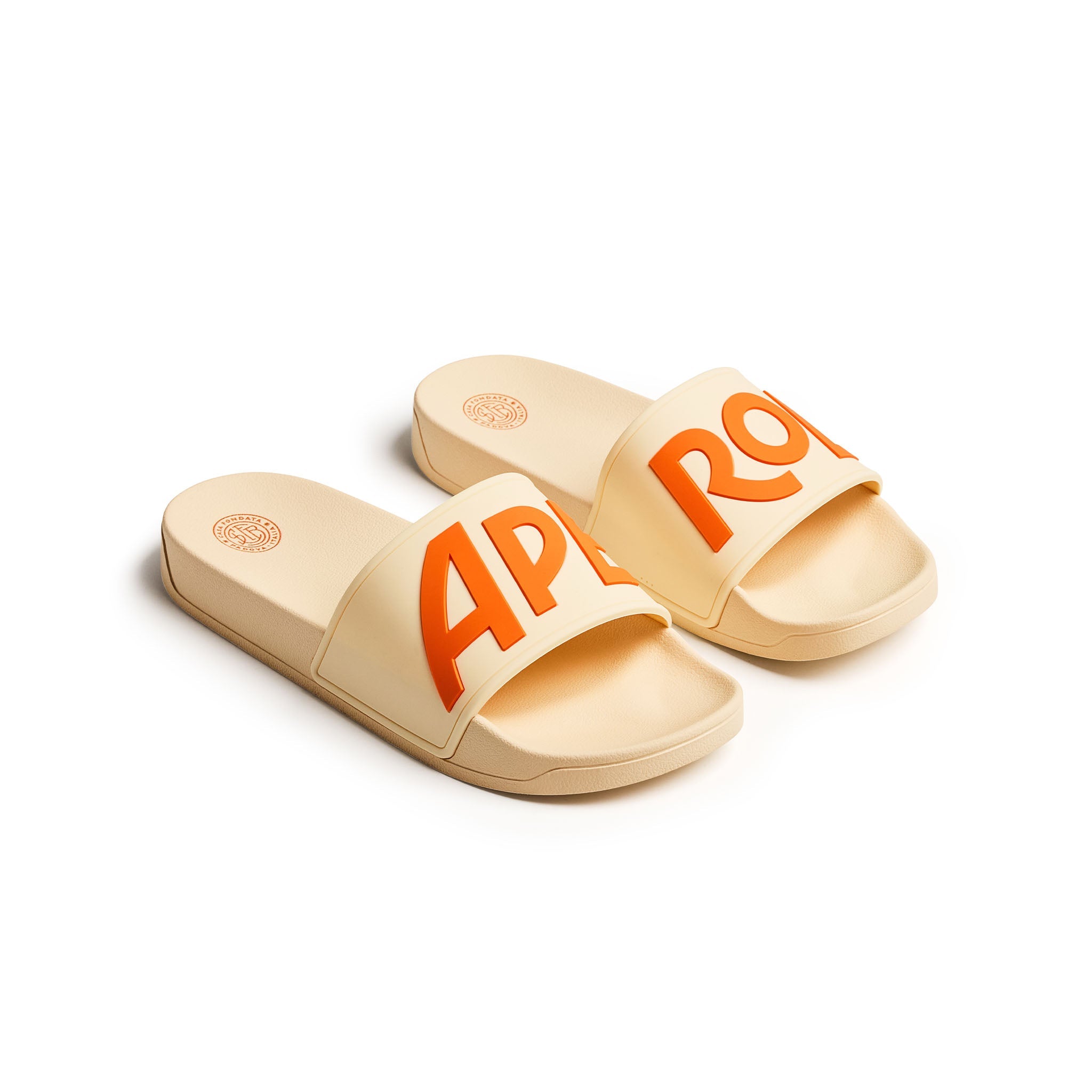 A pair of beige slide sandals with bold orange lettering spelling 'APEROL' across the straps, displayed on a clean white background.