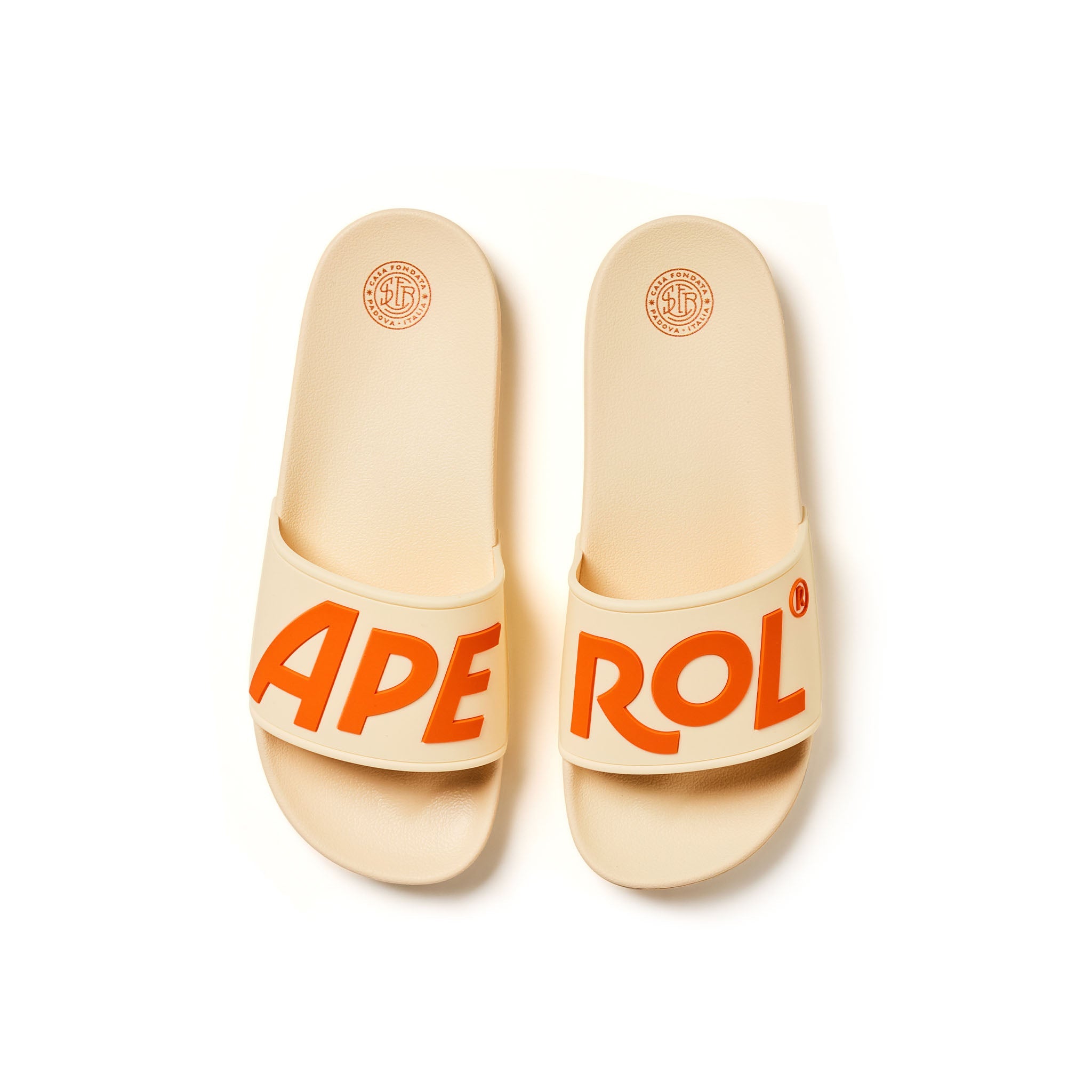 A pair of beige slide sandals with bold orange lettering spelling 'APEROL' on the straps, shown from a top-down view on a white background.