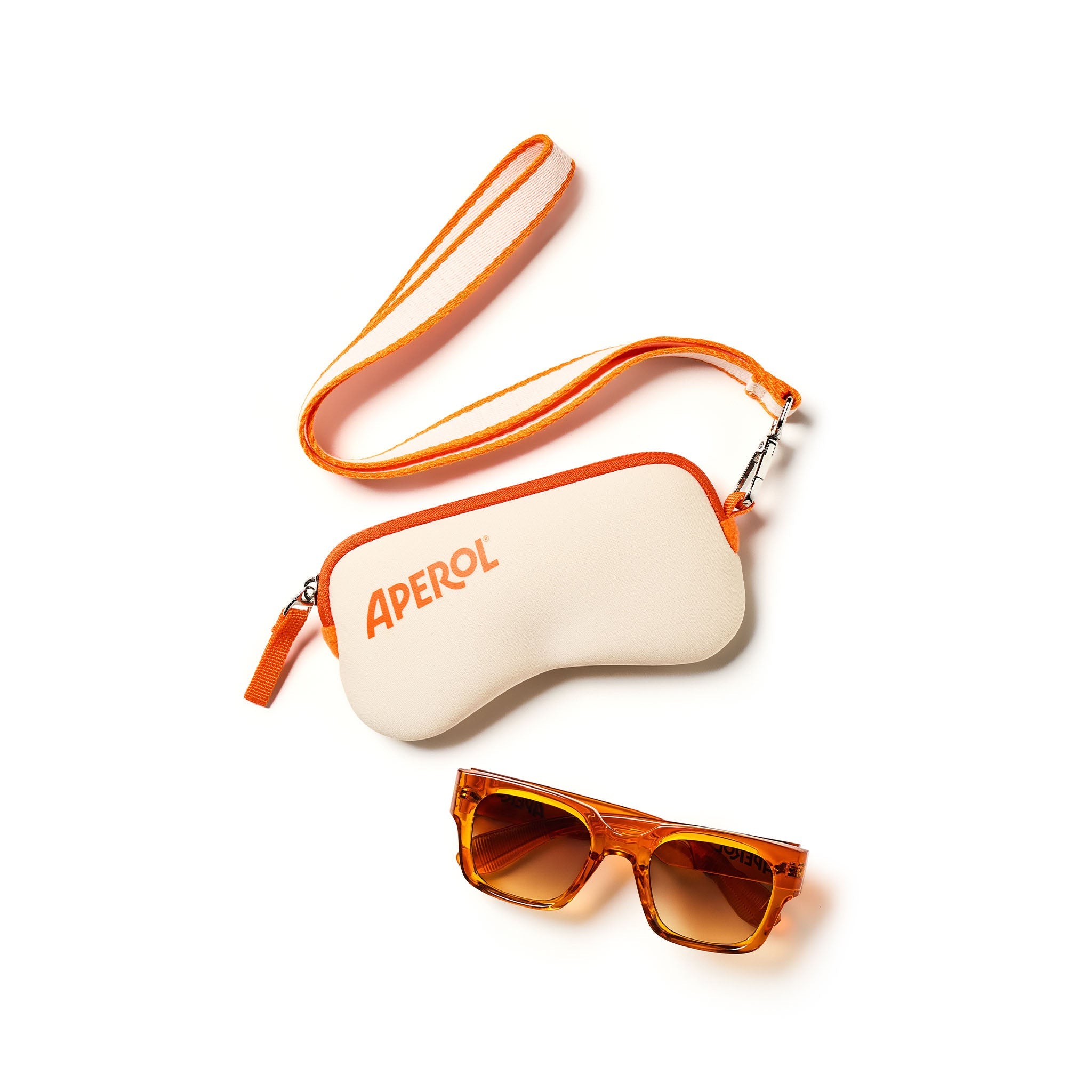 An APEROL sunglasses case in off-white with orange trim and a matching orange-and-white wrist strap, shown with a pair of orange-tinted sunglasses on a clean white background.