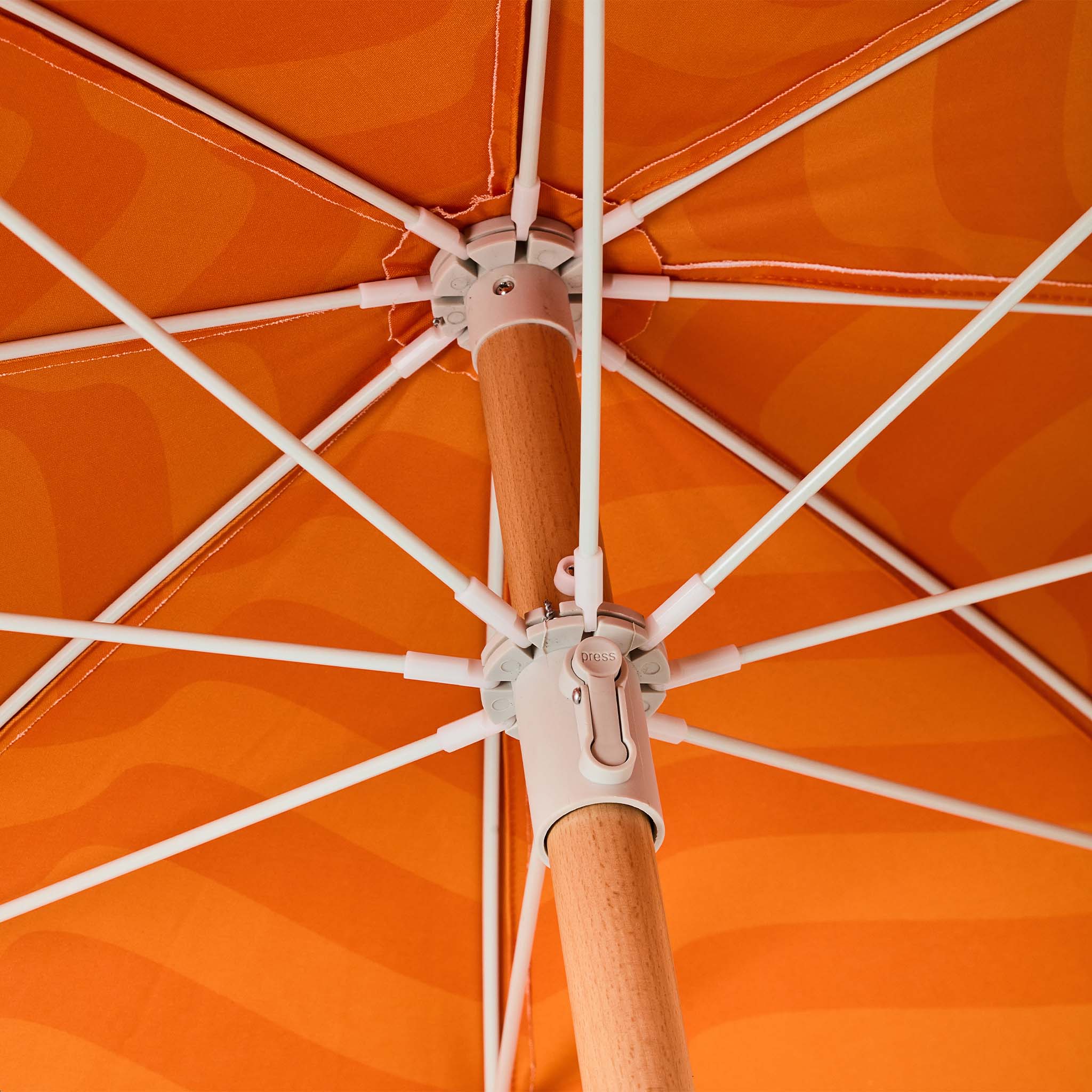 Close-up of the underside of an orange umbrella with white ribs and a wooden central pole.